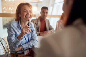 caucasian female boss listening colleague, smiling, laughing, holding glasses