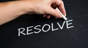 A hand writes the word resolve on a blackboard, symbolizing determination, goal setting, and making a New Year's resolution