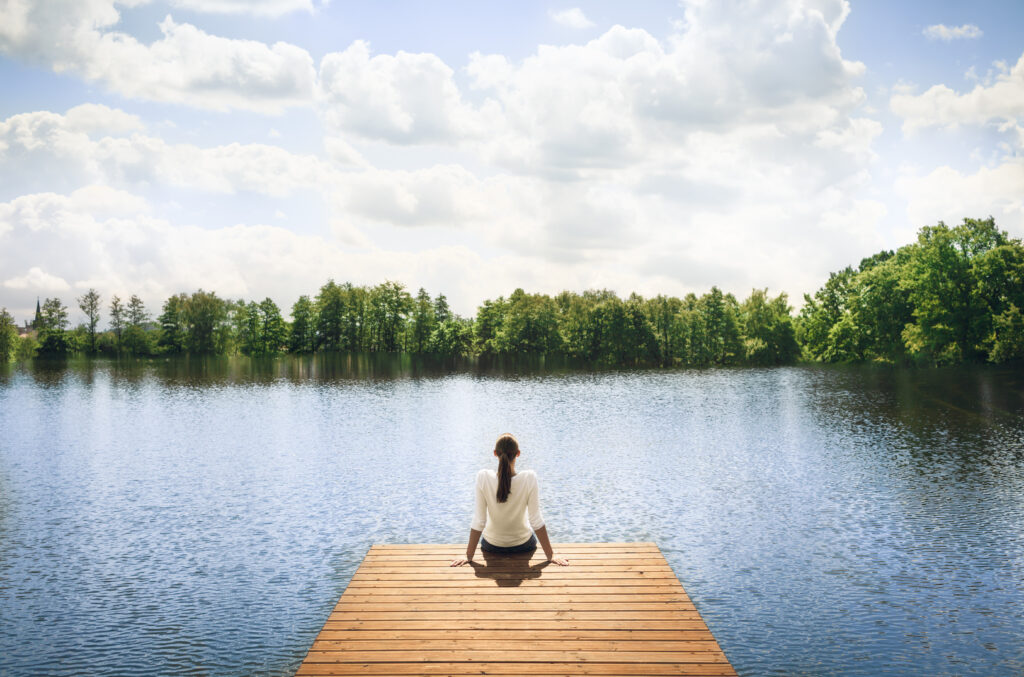 Woman relaxing on wooden dock by a beautiful lake. Peace and tranquility in nature.