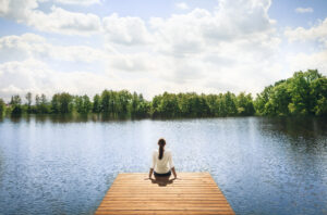 Woman relaxing on wooden dock by a beautiful lake. Peace and tranquility in nature.